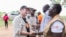 FILE - U.S. Democratic Sen. Chris Coons, left, tours Bidi Bidi in Uganda, one of the largest refugee settlements in the world, Aug. 13, 2019.