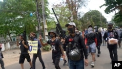 Pengunjuk rasa anti-kudeta berbaris dengan senapan angin rakitan saat salah satu dari mereka memegang tanda yang menunjukkan dukungan untuk tentara federal yang dibentuk sipil selama pawai protes di Yangon, Myanmar, Sabtu, 3 April 2021. (Foto: AP)
