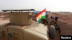 File - A Kurdish flag is seen next to Peshmerga fighters taking position with their weapons on the frontline against the Islamic State, on the outskirts of Mosul, Iraq.