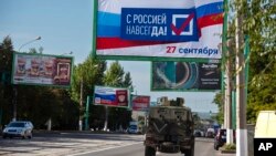 یک خودروی نظامی روسیه در خیابانی در لوهاسنک که در آن تابلوهایی با نوشته «با روسیه برای همیشه، ۲۷ سپتامبر» نصب شده، در روز ۲۲ سپتامبر ۲۰۲۲، پیش از رفراندم. منطقه لوهانسک تحت اشغال روسیه در شرق اوکراین است.