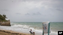 A man sits in front of a beach watching as the waves break before the arrival of Tropical Storm Fiona in San Juan, Puerto Rico, Sept. 17, 2022. 