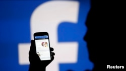FILE - A man is silhouetted against a video screen with an Facebook logo, Aug. 14, 2013. 
