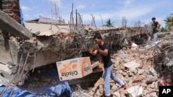 Seorang pria mengambil sebuah kotak makanan dari bawah reruntuhan bangunan pasca gempa yang menghantam wilayah Pidie Jaya, provinsi Aceh, Indonesia, 7 Desember 2016 (AP Photo/Heri Juanda).