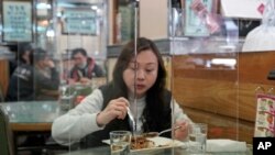 Customer has lunch with a transparent plastic panel setup on the table to isolate her from others in hopes of stopping the spread of the coronavirus in a Hong Kong, Wednesday, Feb. 12, 2020. 