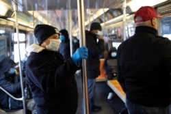 A subway rider wears a glove while holding a pole as several riders wear face masks during the coronavirus outbreak on the D train in the Brooklyn borough of New York on March 25, 2020.