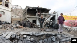 Men stand next to a crater made by a car bomb attack near the presidential palace in the southern port city of Aden, Yemen, Jan. 28, 2016. 