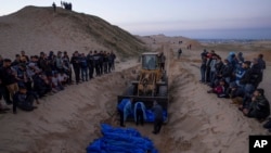 A bulldozer unloads the bodies of Palestinians killed in fighting with Israel and turned over by the Israeli military during a mass funeral in Rafah, Gaza Strip, Dec. 26, 2023.