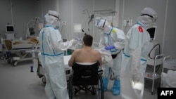 FILE - Medical workers in protective suits treat a patient (not the author of this story) infected with the coronavirus, at a makeshift hospital set up at the Sokolniki Exhibition and Convention Center in Moscow, Russia, Nov. 9, 2020. 