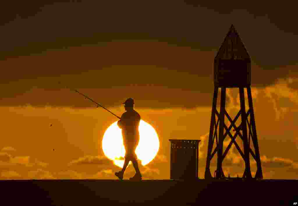 A fisherman on a jetty prepares to cast his line as the sun rises behind him, on the Atlantic Ocean in Bal Harbour, Florida.