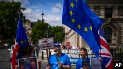 Protesters, one of them holding a photograph of British Prime Minister Boris Johnson and Britain's Home Secretary Priti Patel, stand outside the Houses of Parliament, in London, July 6, 2022.