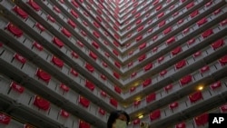 A woman walks past the Chinese and Hong Kong flags hanging from a residential building to celebrate the 25th anniversary of Hong Kong handover to China, at a public housing estate, in Hong Kong, Saturday, June 25, 2022.
