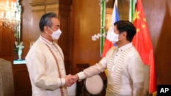 In this photo provided by the Malacanang Presidential Photographers Division, Philippine President Ferdinand Marcos Jr., right, greets Chinese Foreign Minister Wang Yi as he arrives for a courtesy call at the Malacanang Presidential Palace in Manila, Phil
