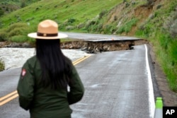 FILE - A Yellowstone National Park ranger stands near a road wiped out by flooding along the Gardner River, near Gardiner, Mont., June 19, 2022.