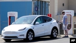 FILE - A Tesla owner charges his vehicle at a charging station in Topeka, Kansas, April 5, 2021.