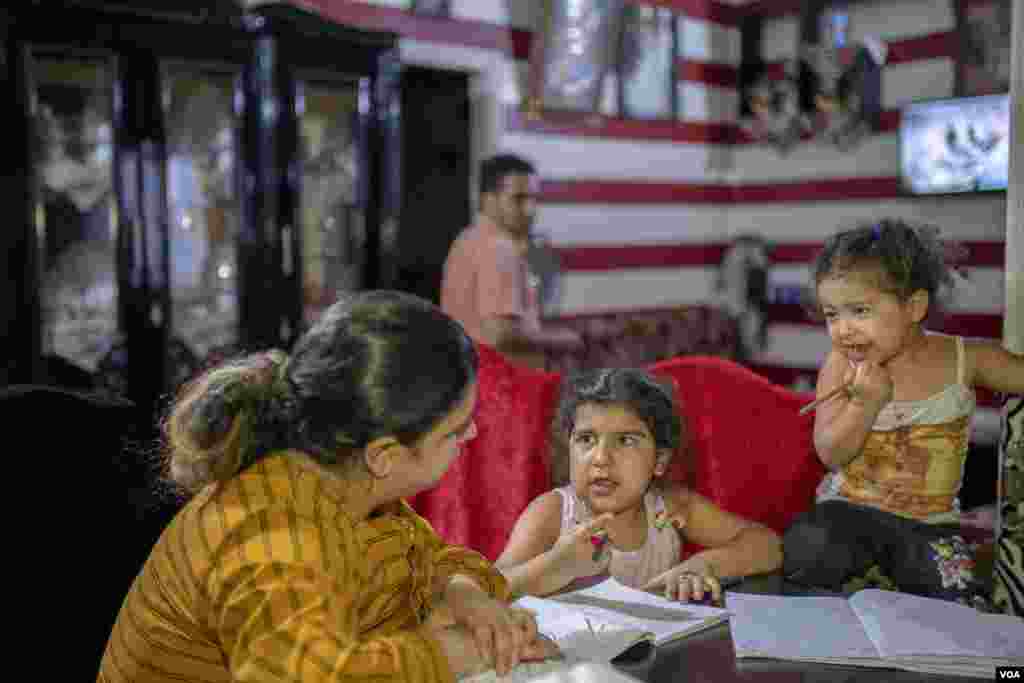 As dinner boils on the stove, Marina helps one daughter with her homework and teaches the alphabet to the other, in Cairo, June 26, 2022. 