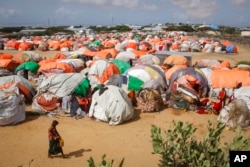 FILE - Somalis who fled drought-stricken areas walk next to a cluster of makeshift shelters at a camp for the displaced on the outskirts of Mogadishu, Somalia, June 4, 2022.