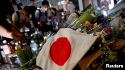 A Japanese flag is seen as people pray next to tributes laid at the site where late former Japanese Prime Minister Shinzo Abe was shot while campaigning for a parliamentary election, near Yamato-Saidaiji station in Nara, western Japan, July 8, 2022.