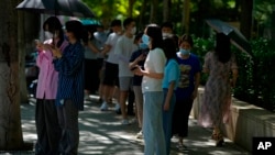 Residents stand in shade to avoid the sun's heat as they line up for coronavirus tests in Beijing, July 7, 2022. The Chinese capital is requiring people to show proof of COVID-19 vaccination before they can enter some public spaces.