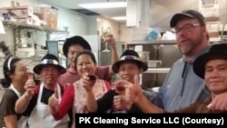 ເຈົ້າຂອງບໍລິສັດ ນາງບົວສອນ ສຸນາເຄນ, ໃສ່ເສື້ອສີແດງ ຢືນຢູ່ທາງກາງ, ແລະພະນັກງານຂອງລາວ ພາກັນຖ່າຍຮູບຢູ່ທີ່ເຮືອນຄົວຂອງຮ້ານອາຫານແຫ່ງນຶ່ງ.