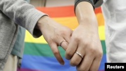 FILE - Plaintiffs hold each others' hands after a district court ruled on the legality of same-sex marriages, outside Sapporo district court, in Sapporo, Hokkaido, northern Japan, March 17, 2021. (Kyodo/via Reuters)