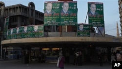 An Egyptian woman walks under electoral posters supporting the ruling National Party with a picture of Gamal Mubarak, son of President Hosni Mubarak, ahead of the upcoming Nov. 28 parliamentary elections, in Alexandria, Egypt, 27 Nov 2010