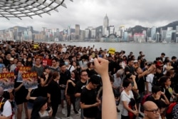 FILE - Protesters march near the skyline of Hong Kong, July 7, 2019. China’s central government has dismissed Hong Kong pro-democracy protesters as clowns and criminals while bemoaning growing violence surrounding the monthslong demonstrations.