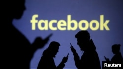 FILE - Silhouettes of mobile users are seen next to a screen projection of Facebook logo in this picture illustration taken March 28, 2018.