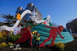 Workers wearing face masks to help protect from the coronavirus set up a decoration for the Winter Olympic Games in Beijing, Jan. 16, 2022.