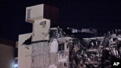 A firefighter shines a flashlight at far left as they search a building after a partial collapse, June 24, 2021, in the Surfside area of Miami, Fla. 