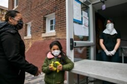 Allison, 5, holds two bananas next to her mother Janeth, left, as a volunteer at the food bank Martha's Table waits to help the next guest, April 21, 2020, in Washington.