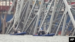 Barcos de la policía trabajan alrededor de un carguero atrapado bajo una parte de la estructura del puente Francis Scott Key, el miércoles 27 de marzo de 2024, en Baltimore, un día después de que el carguero chocó contra una columna del puente y causó su derrumbe. 