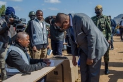 FILE - Then-President Peter Mutharika gets instructions on how to vote from a presidisng officer, in Thyolo district. (Lameck Masina/VOA)