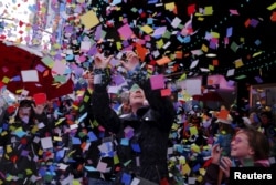 FILE - Pedestrians watch confetti fall as members of the Times Square Alliance perform an "air worthiness test" for the confetti that is similar to what will be used for New Year's Eve in New York on Dec. 29, 2015.