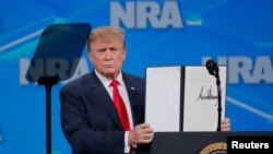 President Donald Trump holds up an executive order as he announces that the United States will drop out of the Arms Trade Treaty, April 26, 2019.