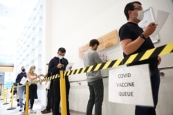 FILE - People queue to receive a dose of the Pfizer BioNTech vaccine at the Central Middlesex Hospital in London, Britain, Aug. 1, 2021.