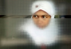 Seorang buruh migran melihat dari balik pintu kaca sambil menunggu dokumennya diproses setelah tiba dari Malaysia, di terminal khusus buruh migran di Bandara Soekarno-Hatta, Jakarta, 28 Oktober 2009. (Foto: REUTERS/Beawiharta )