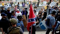 FILE - A white supremacists carries the Confederate flag as he walks past counter-demonstrators in Charlottesville, Virgina, Aug. 12, 2017.
