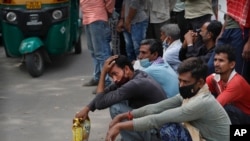 Migrant laborers Nirbhay Yadav, 50, wearing checked scarf, and his son Lovelesh Yadav, left, wait to get employed for the day in New Delhi, India, March 18, 2021.