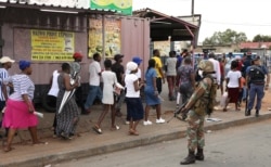 FILE - A member of the South African National Defense Force keeps watch as shoppers leave a grocery store, after being ordered by law enforcement during a lockdown to contain the coronavirus disease, in Alexandra, South Africa, March 27, 2020.