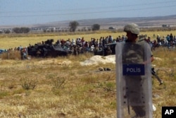 Turkish soldiers stand as people from the Syrian town of Ain al-Arab, or Kobani, wait to cross into Turkey following the attacks by Islamic State militants as seen from the Turkish side of the border in Suruc, Turkey, June 25, 2015.