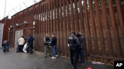 ARCHIVO - Agentes federales les quitan las esposas a hombres antes de liberarlos a través de una puerta en un muro fronterizo con Tijuana, México, el miércoles 15 de marzo de 2023, en San Diego.