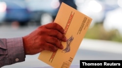 FILE - An election worker places a mail-in ballot into an election box at a drive-through drop-off site at the Registrar of Voters in San Diego, California.