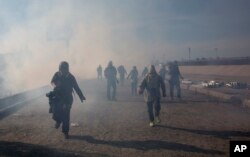 FILE - Migrants run from tear gas launched by U.S. agents, amid photojournalists covering the Mexico-U.S. border, after a group of migrants got past Mexican police at the Chaparral crossing in Tijuana, Mexico, Nov. 25, 2018.