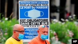 People wearing face masks walk past a sign stating face coverings are required in the street, in Bayonne, southwestern France, July 28, 2021. 