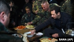 Making a rare visit to the front line, Syrian President Bashar Assad, right, shares a meal with Syrian troops during his visit on the front line in the eastern Damascus district of Jobar, Syria, Dec. 31, 2015. 