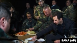 President Suriah Bashar al-Assad (kanan) berbagi makanan dengan tentara Suriah di garis terdepan, saat meninjau mereka di distrik Jobar, Damaskus, Suriah (31/12).