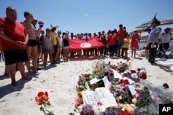 People, some displaying a Tunisian flag, stand in silence next to flowers during a gathering at the scene of the attack in Sousse, Tunisia, June 28, 2015.