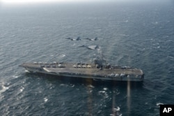 In this Nov. 10, 2017, photo provided by Japan's Air Self-Defense Force, two U.S. F/A-18s and Japanese F-15s fly over the USS Ronald Reagan toward a joint military exercise at an undisclosed location.