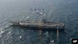 FILE - In a photo provided by Japan's Air Self-Defense Force, two U.S. F/A-18s and Japanese F-15s fly over the USS Ronald Reagan toward a joint military exercise at an undisclosed location, Nov. 10, 2017.