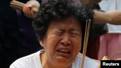 A family member of a passenger aboard the missing Malaysia Airlines flight MH370 cries as she burns incense to pray at Yonghegong Lama Temple in Beijing, June 15, 2014. 